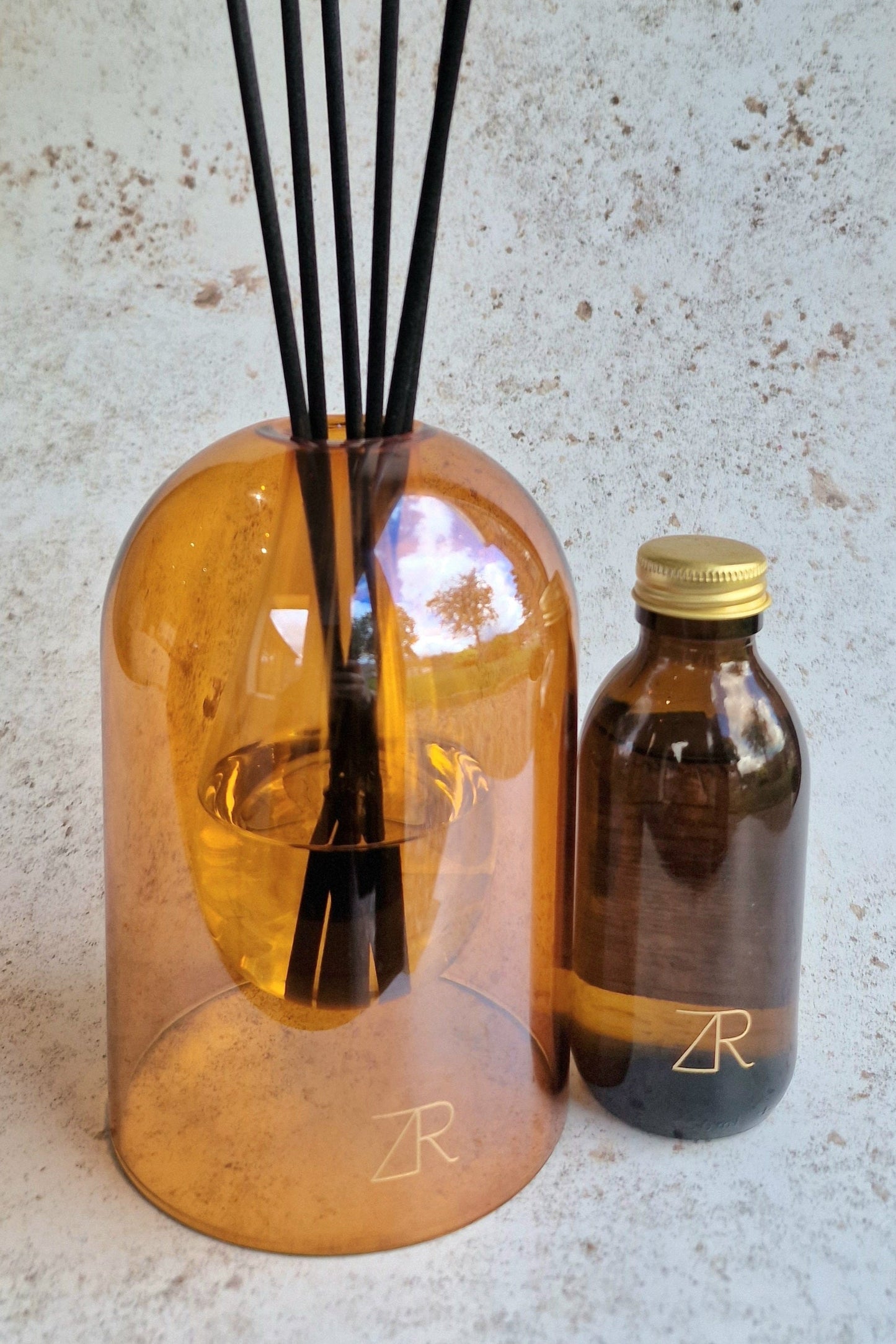 A diffuser bottle with black sticks and a smaller bottle on a textured surface