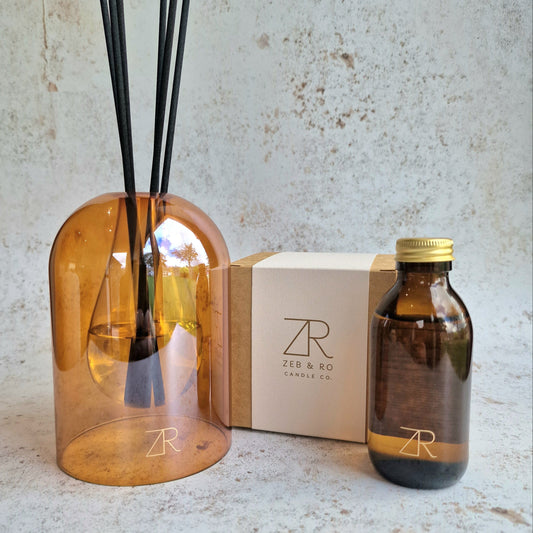 Aromatherapy diffuser set with amber glass and black reeds, a box, and a smaller bottle on a textured surface.